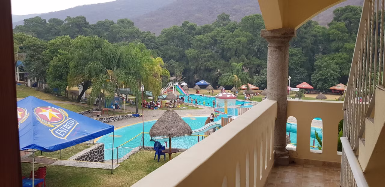 Vista del balneario con albercas, palapas y montañas al fondo